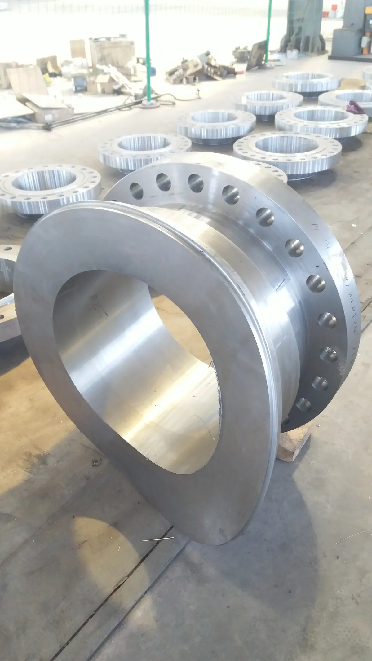 A large machined long weld neck flange lying on its side, with a barrel ending in a curved (saddle-contoured) weld end