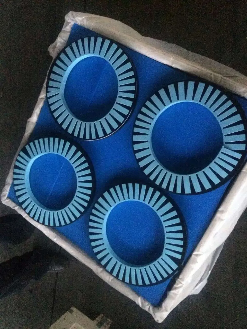 Four slotted rings, radial slots around their outer edge, laid on blue foam in a crate lined with white plastic film