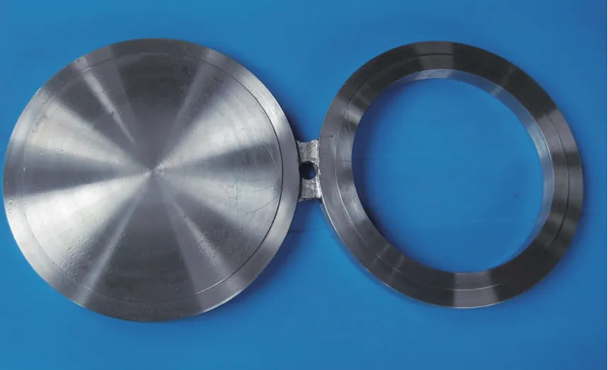 A figure-8 (spectacle) blank on a blue sheet: a solid machined disc and an open ring joined by a short web