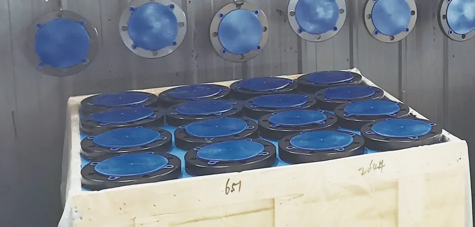 Black-coated flanges with blue plastic face covers, some hanging on a wall line and others packed covers-up in an open wooden crate