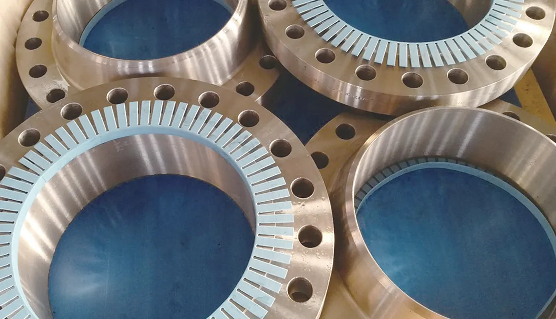 Large machined weld neck flanges with an oiled, coppery sheen lying together; light-blue slotted rings lie on the faces of two of them