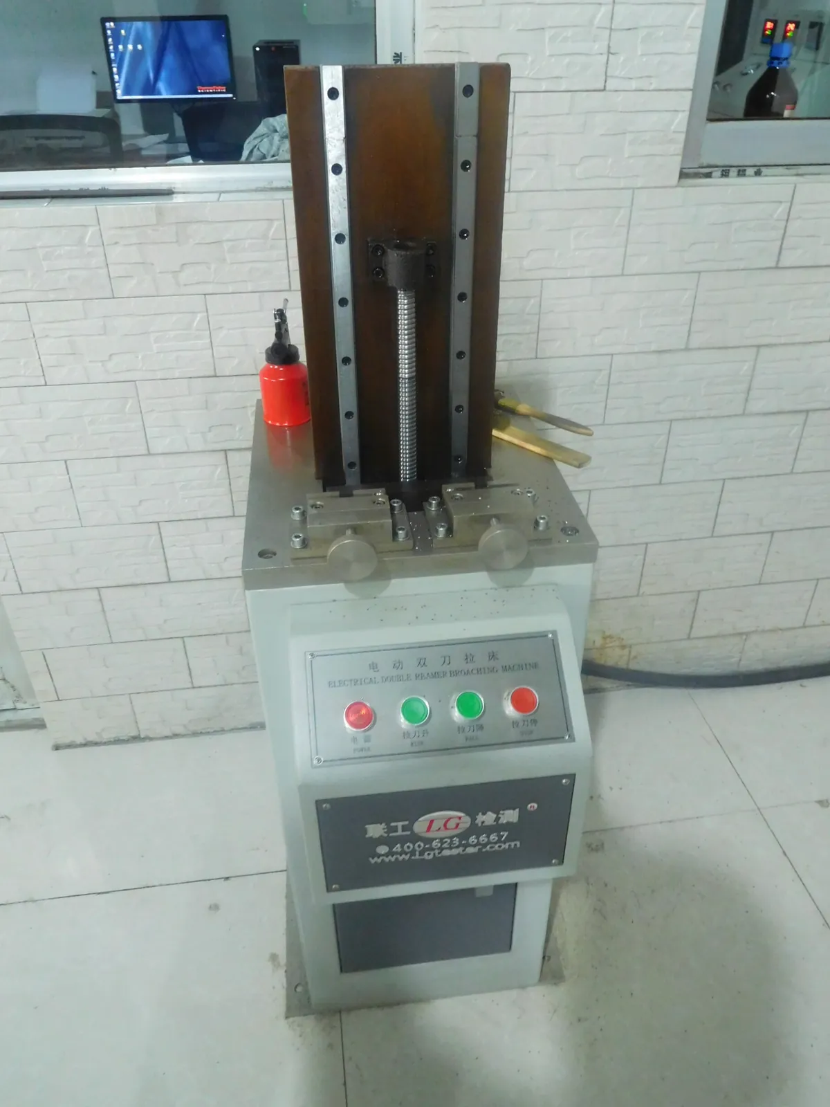 Small vertical broaching machine with a push-button control box, standing in a tiled lab room