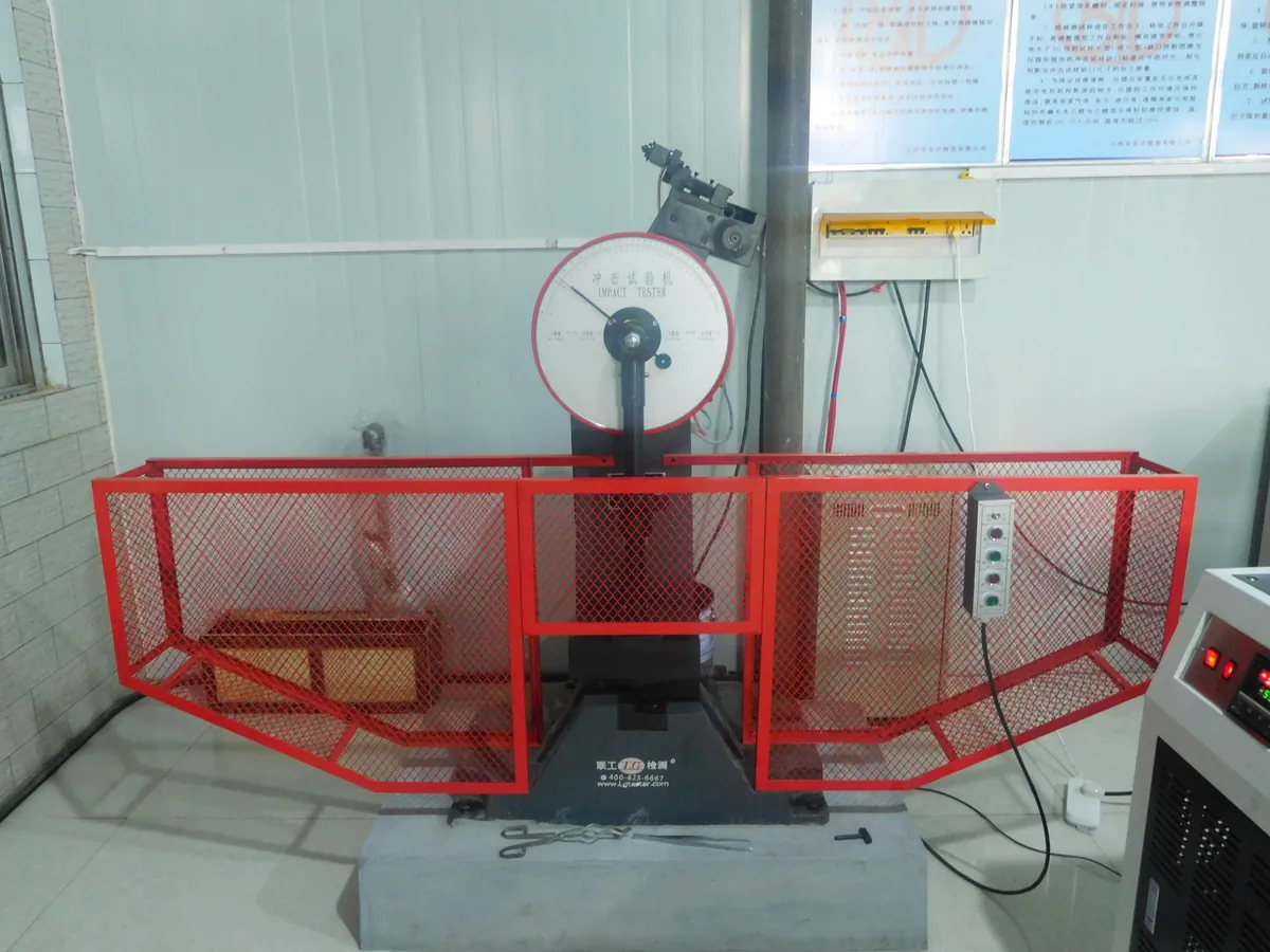 Pendulum impact testing machine behind a red mesh safety guard in a lab