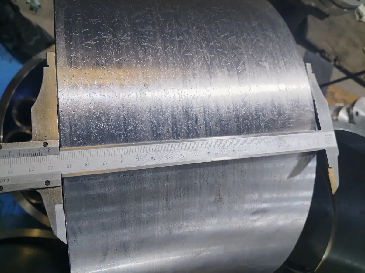 A vernier caliper spans the length of a large machined ring lying on its side, jaws on both end faces