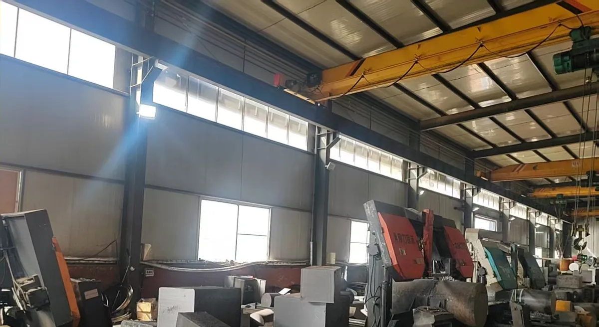 Inside a hall with large band-saw machines with red covers, cut steel blocks and bar ends on the floor, and overhead cranes