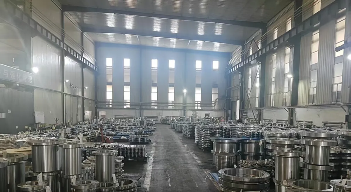 A tall warehouse aisle lined with hundreds of machined flanges, including flanges with long cylindrical hubs