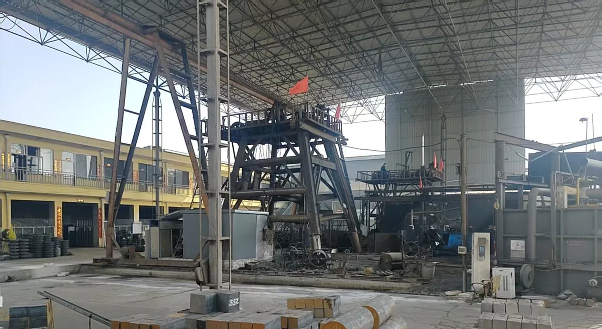 An open forging hall under a steel space-frame roof, with a tall press tower and a heating furnace