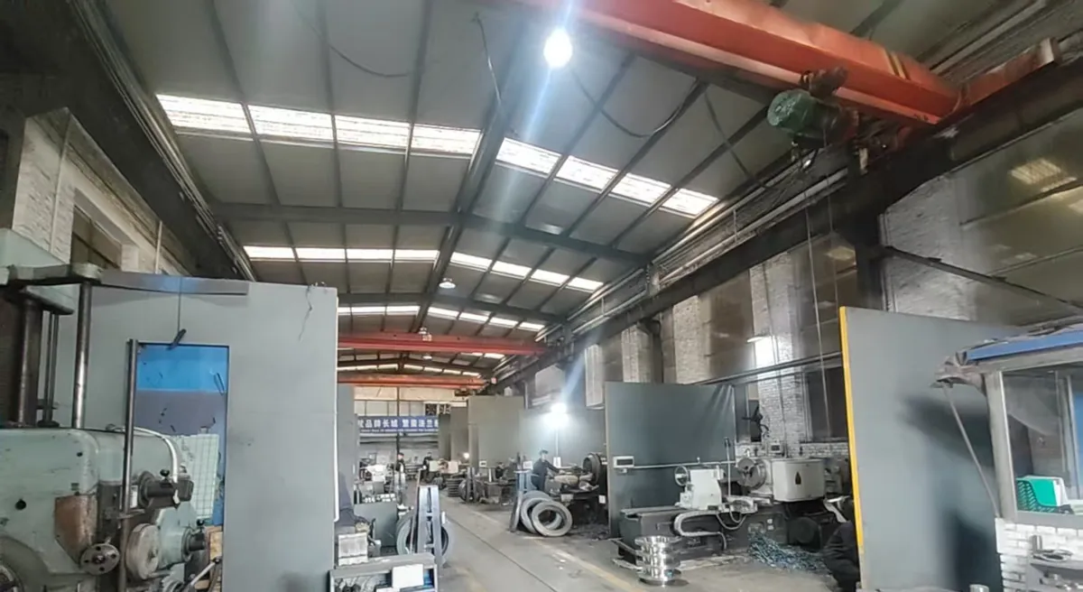 Long brick machining hall with rows of lathes and machine tools on both sides and a red overhead crane