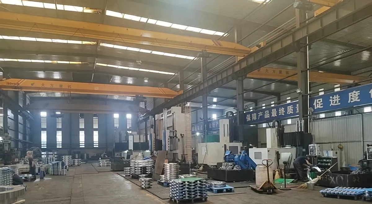 Large machining hall with yellow overhead cranes, large CNC machines on the right and pallets of machined flanges