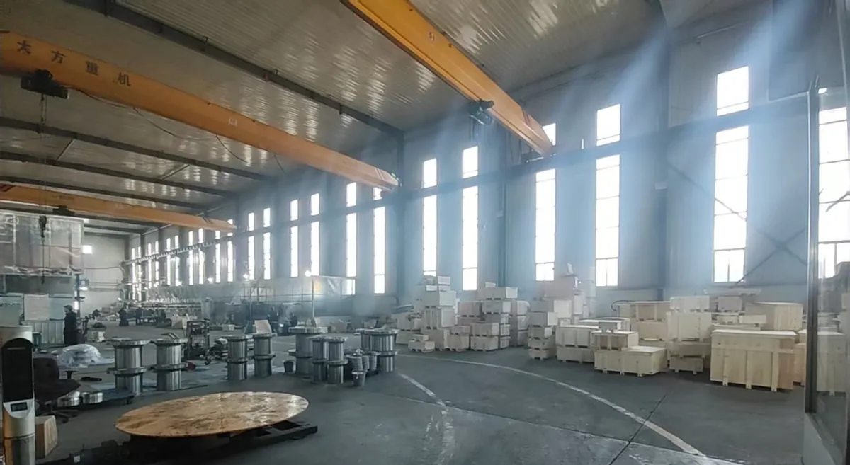 Large bright hall with overhead cranes, rows of flanges with long hubs and many plain wooden crates on the right